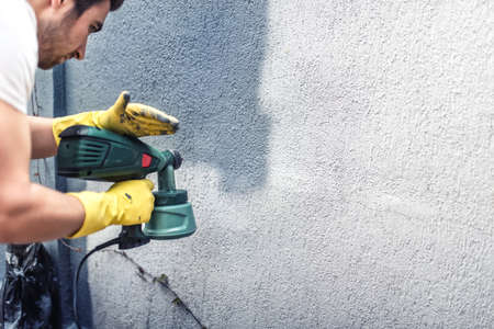 Man painting a grey wall, renovating exterior walls of new houseの写真素材