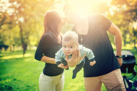Happy father holds newborn baby on arm while kissing the mother of child. happy family in park, newborn kid and happinessの写真素材