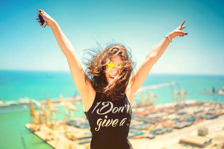 Attractive girl wearing black tank top smiling, laughing and taking pictures with camera phone. Traveling concept with happy woman. Soft colorful effect on photoの写真素材