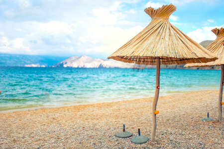 beach straw umbrella lounger chair with sand and clear water. Sea mediteraneean coastline landscapeの写真素材