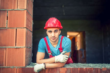 portrait of industrial worker on construction site, sitting and relaxing after a hard day at work. Brick mason worker with protective gearの写真素材