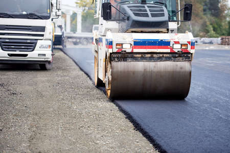 Road works, asphalting and laying fresh bitumen during construction works. Industrial heavy duty...
