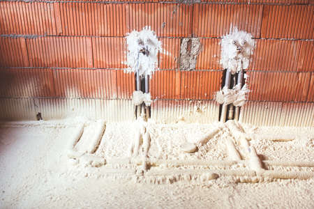 thermal insulation with spray foam, brick walls and pipes at construction siteの写真素材