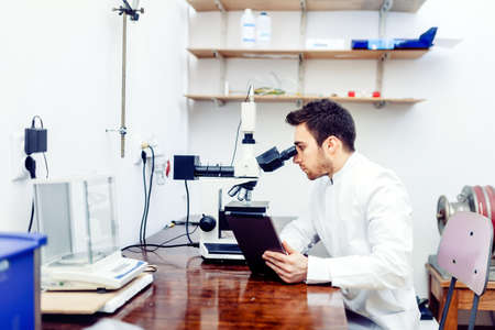 Pharmacist and medical scientist looking at tablet and comparing microscope results from sample experimentsの写真素材