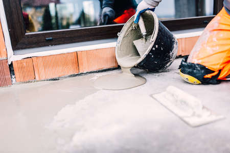 industrial worker on construction site pouring sealant from bucket for waterproofing cementの写真素材