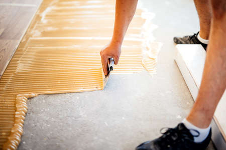 industrial worker adding glue on cement floor, preparing surface for wood parquetの写真素材