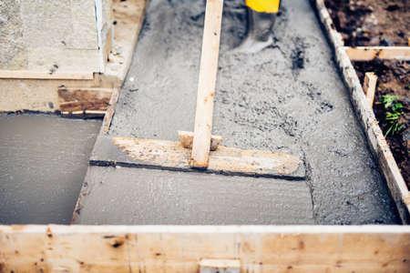 Mason building and leveling a first layer of fresh concrete floor at house stairs and sidewalks, construction siteの写真素材