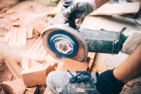 worker using grinder on construction site for cutting bricks, debris. Tools and bricks on new building siteの写真素材
