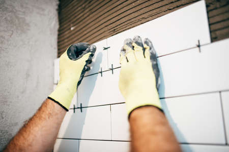 Industrial worker using plastic distancer for adjusting ceramic tiles on bathroom walls
