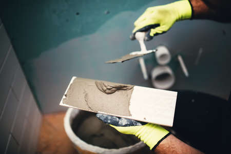 industrial close up detail of worker adding cement adhesive on small ceramic tiles