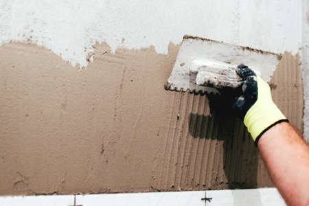 industrial close up of worker hand adding cement adhesive for ceramic tiles installationの写真素材