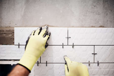 industrial worker installing small ceramic tiles in bathroom during renovation worksの写真素材