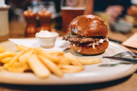 Tasty grilled beef burger with lettuce and mayonnaise served on white plate with french fries. modern dinner with burger and friesの写真素材