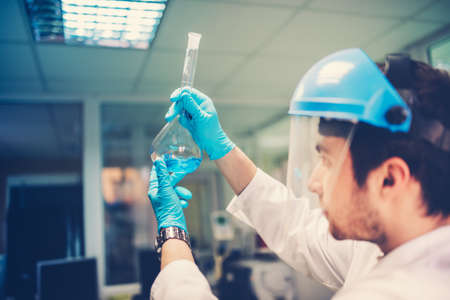 Flask test tube in scientist hands. Details of young doctor analyzing composition and structure of blue liquidの写真素材