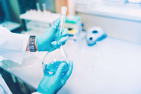 Doctor holding a glass test tube, a flask with blue liquid in special laboratory preparing for experimentsの写真素材