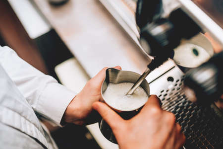 Professional bartender warming milk for cappuccino. Barista using coffee machine for latte art macchiato. Toned imageの写真素材