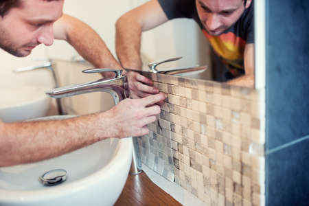 Handyman using adhesive cement for installing ceramic mosaic tiles. Details of renovationの写真素材