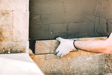 Close up details of worker hands using cement and mortar and installing stone on vertical wallsの写真素材