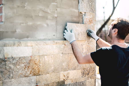 Construction industry worker installing stone tiles on architectural house facadeの写真素材