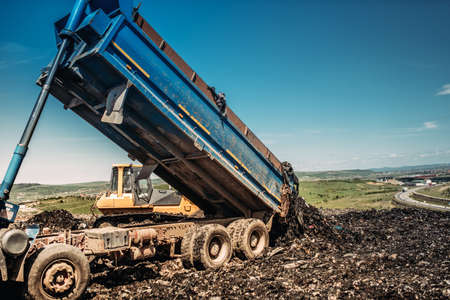 industrial dumper trucks unloading garbage into trash hillの写真素材