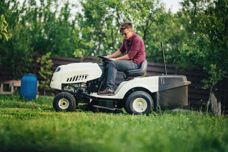 Worker using lawn mower for cutting grass in gardenの写真素材