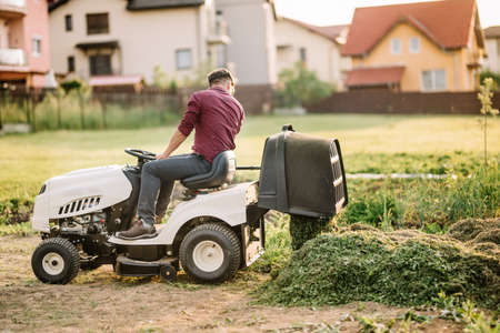 professional gardner unloading cut grass from containter. Worker using machinery for landscapingの写真素材