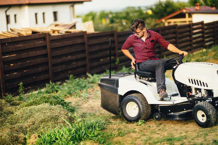 Man with lawn mower, professional worker cutting and unloading grass