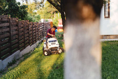 male worker riding lawn mower and trimming grass in gardenの写真素材