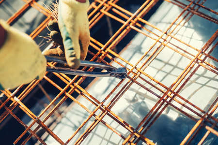 Construction site details with worker using wire rod and pliers for securing reinforcement steel...
