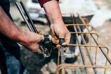 worker hands using steel wire and pincers to secure steel bars, preparing for concrete pouring on indutrial construction siteの写真素材