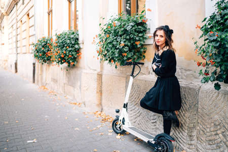 urban lifestyle details - happy woman standing on an alley with flowers and electric kick scooterの写真素材