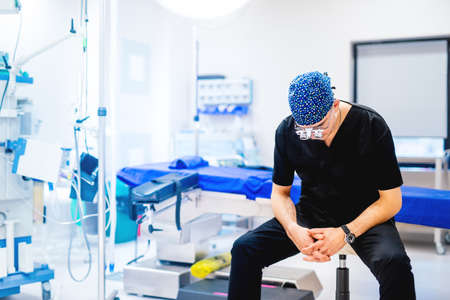 Professional surgeon sitting in operating room with empty table and no scrubs