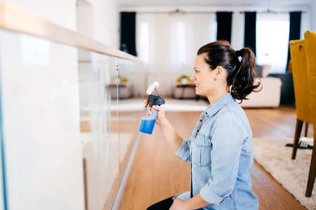 Close up portrait of modern woman doing housework around the house. Woman cleaning glass with...
