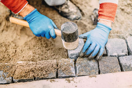 Construction worker placing stone tiles, cobblestone blocks in sand. Portrait of industrial workerの写真素材