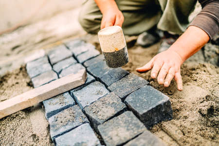 Male construction worker using granite cobblestone blocks to create path or sidewalkの写真素材