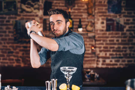Lifestyle details with barman portrait using shaker and preparing cocktail at barの写真素材