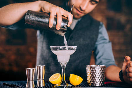Professional bartender pouring margarita cocktail with strainer and cocktail toolsの写真素材