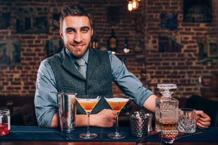 Handsome smiling bartender enjoying work and preparing cocktails at barの写真素材
