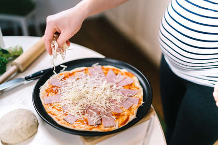 Pregnant woman cooking, putting cheese and mozzarella on pizzaの写真素材