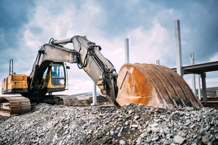 Industrial heavy duty excavator moving gravel on highway construction site. Multiple industrial...