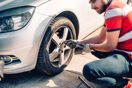 Tire maintenance, damaged car tyre or changing seasonal tires using wrench. Changing a flat car tire on the sideroad or in the courtyardの写真素材