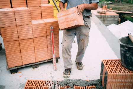 Industrial worker moving bricks and using tools for building exterior walls with bricks and mortarの写真素材