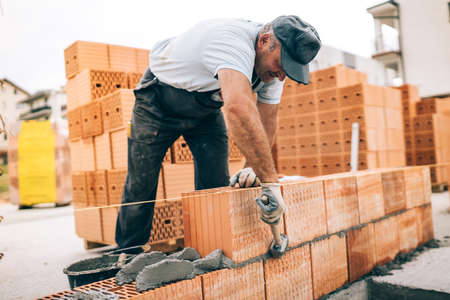 industrial worker building exterior walls, using hammer for laying bricks in cement. Detail of worker with tools and concreteの写真素材