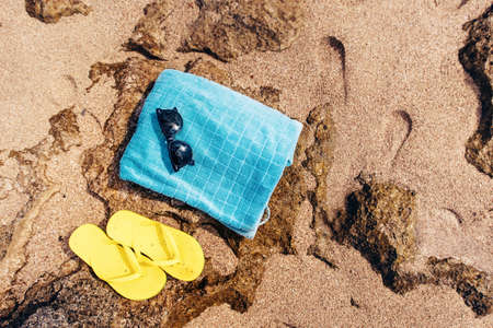 Sunglasses, yellow flip flops, blue towel ready for sunbathing on a sunny afternoon. at beachの写真素材