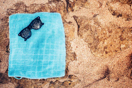 Towel and sunglasses on a sandy background, fashion elements on beach day. Sandy rocks, waves and beach wallpaperの写真素材