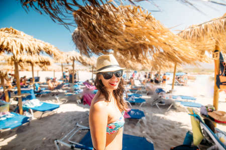 woman in swimsuit, wearing sunglasses and straw hat smiling on tropical beachの写真素材
