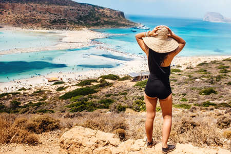 Rear view of beautiful woman wearing one piece swimsuit on island looking at sea and beach, portrait...