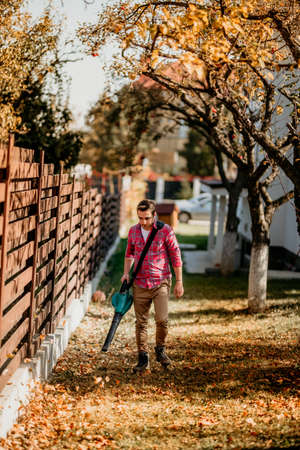 Professional gardener using leaf blower during autumn cleaning. Sunny days in horticulture industryの写真素材
