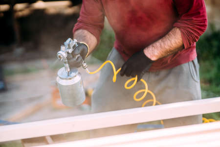 Construction worker painting timber with spraygun, airgun. Carpentry detailsの写真素材