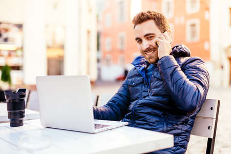 Young smiling man talking on mobile phone while working from outdoor office and staying connected...